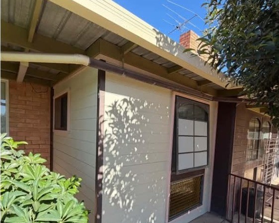 After: the same wall re-clad in clean white weatherboard with fresh trim and eaves.