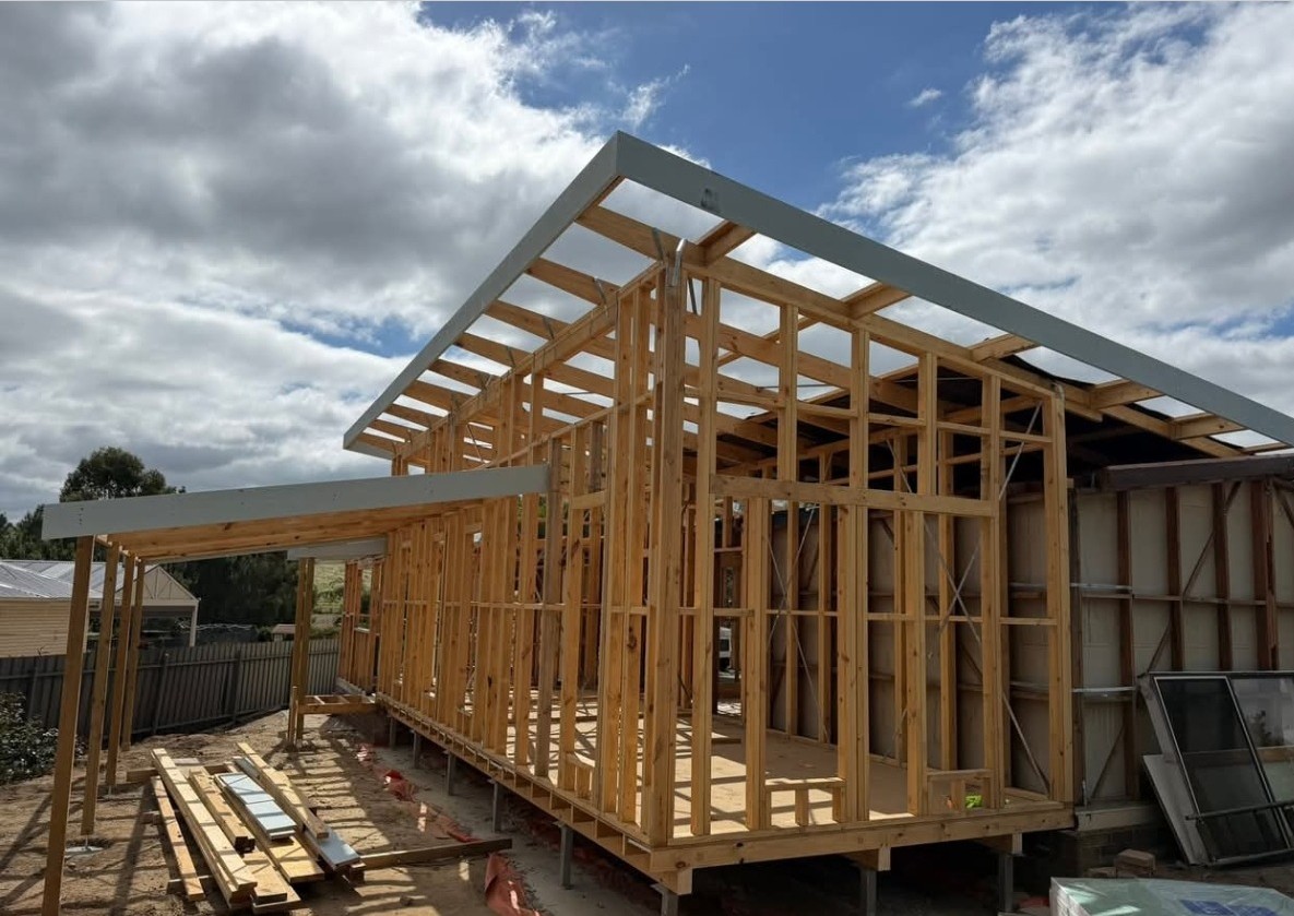 Timber wall and roof framing for a house extension, with steel beams and bracing set out on new footings.