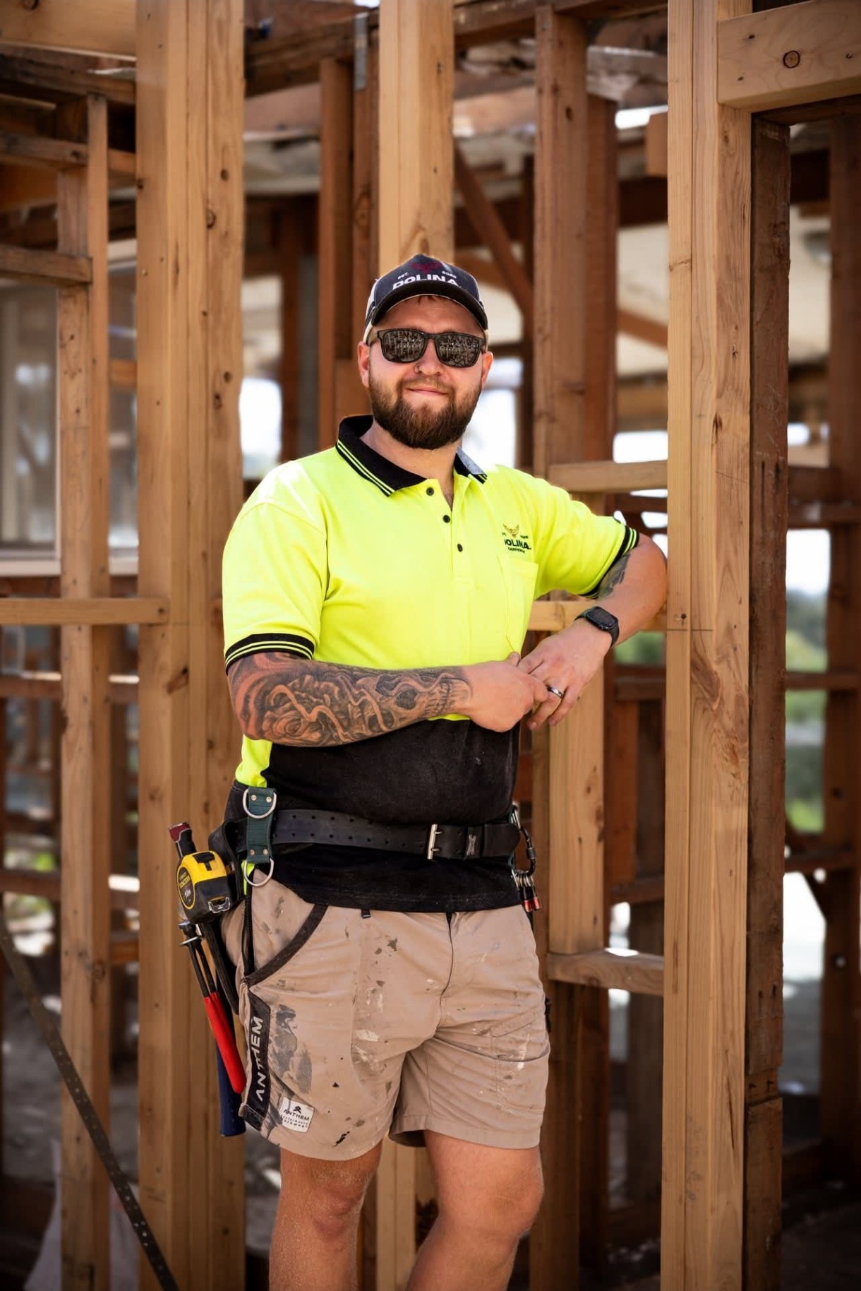 Milosz Gadzinski of Dolina Carpentry on site, in hi-vis and tool belt, leaning against timber framing.